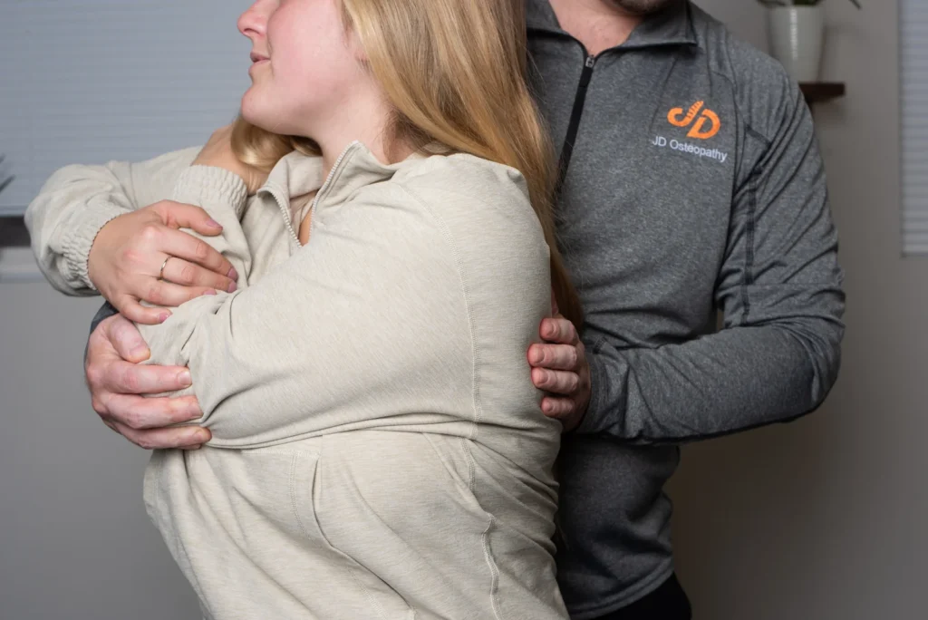 Photo of Dmitro Jovnyruk from JD Osteopathy Treating a patient's rib pain using their arm as a lever in seated position