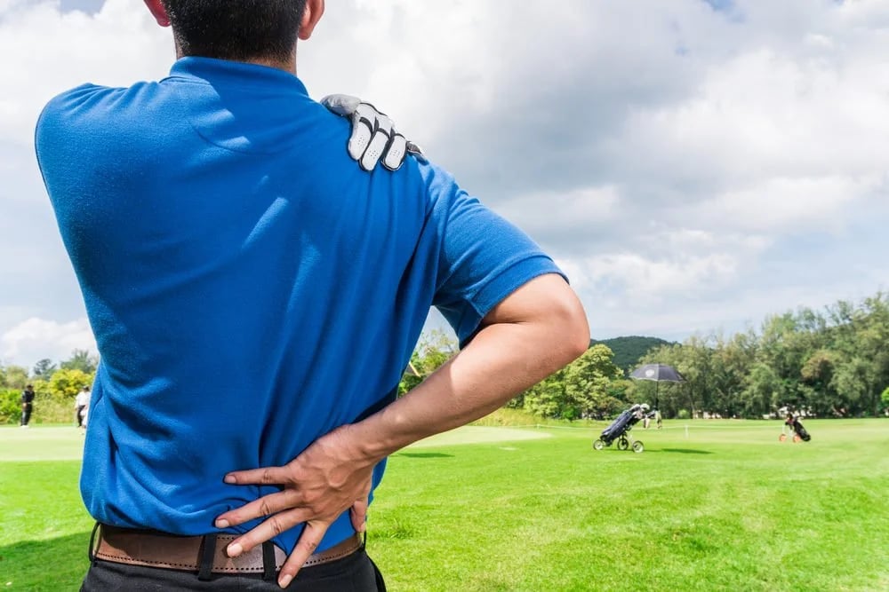 Photo of a golfer holding his back with one hand and shoulder with another hand for golf swing pain
